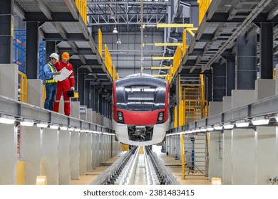 Electric train technician engineer with blueprints  checking controls system for security functions in maintenance infrastructure plant of sky train, public transportation vehicle,Teamwork management