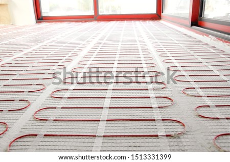 Electric underfloor heating red mats on cement floor. Heating red electrical cable on cement floor copy space background. Renovation and construction, comfortable warm home concept.