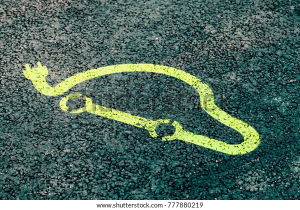Electric vehicle charging point logo painted to\
the asphalt with green paint. Sign on asphalt. Selective focus and\
color effect.
