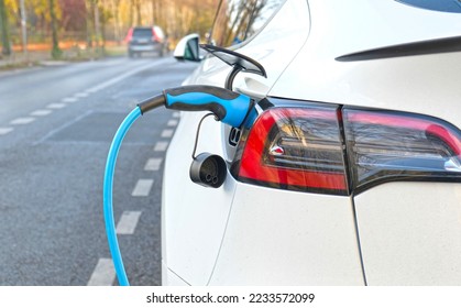 Electric vehicle charging at a public charging station in a city setting. New energy vehicles, eco-friendly alternative energy for cars. Electric cars are becoming more common and gaining popularity. - Shutterstock ID 2233572099