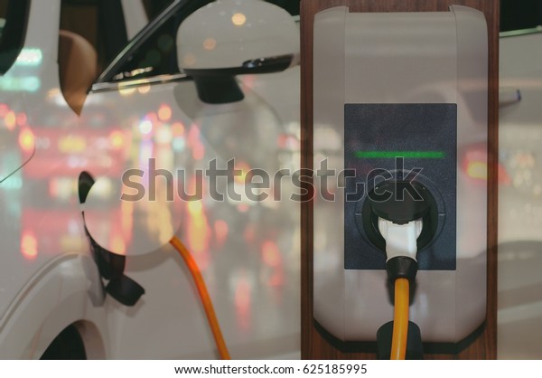 Electric vehicle , Smart car , Air pollution and
reduce greenhouse gas emissions concept. Double exposure of
charging Electric car with power cable supply plugged in and
traffic night light
view.