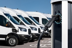 Electric Vehicles Charging Station On A Background Of A Row Of Vans. Green Transportation Concept
