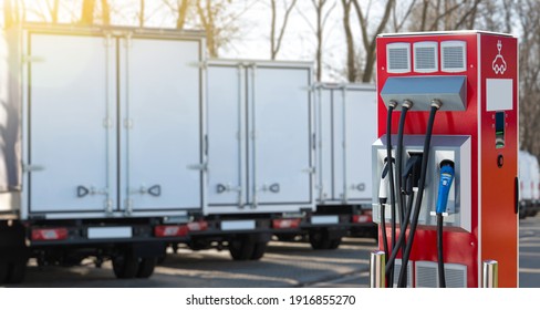 Electric Vehicles Charging Station On A Background Of A Row Of Trucks. Concept