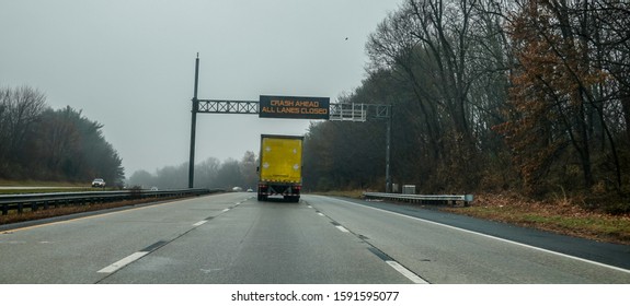 Electric Warning Sign Over Yellow Box Truck On Highway Warning Of Crash Ahead And That All Lanes Are Closed