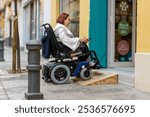 Electric wheelchair user successfully navigates a wooden ramp to access a store, demonstrating accessible architecture.