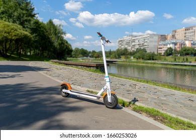 An electric white scooter stands on the bandwagon on the street. City park along the promenade. Sunny summer day. Modern city transport. - Shutterstock ID 1660253026