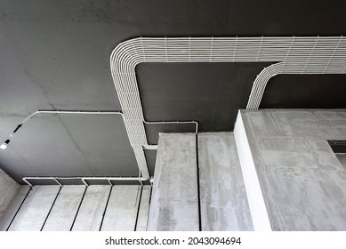 Electrical cables and pipes on house concrete ceiling. Modern plastic hoses and conduits with wires in room. Lines of pvc wiring tubes after professional work. Renovation of home or factory interior. 