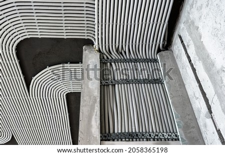 Electrical cables and pipes on house concrete wall and ceiling. Modern plastic hoses and conduits with wires in room. Lines of pvc wiring tubes after professional work. Renovation of home interior.