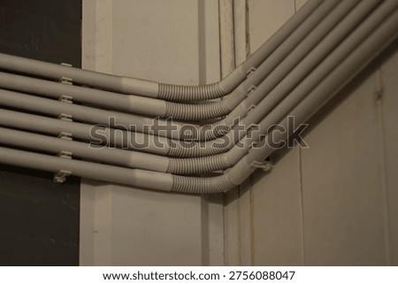 Electrical cables in protective conduits installed along wall inside building.