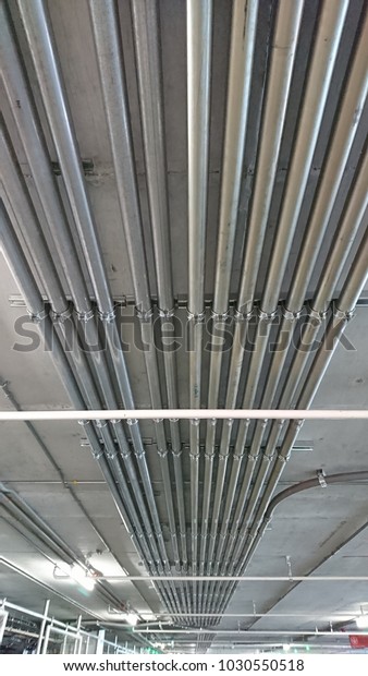 Electrical conduits,\
pipes of power lines and signal cables on congrete ceiling in\
building parking car