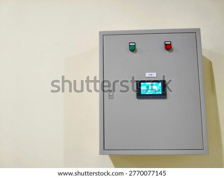 Electrical control panel box with HMI touch screen display and indicator lights on white wall