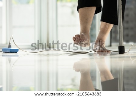 Electrical cord or socket cluttered on the floor,feet of senior woman stepping over obstacles,elderly people walking with difficulty in home,concept of danger,injury and risk of accident in falling