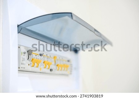 Electrical distribution board featuring multiple circuit breakers and a transparent protective cover, mounted on a wall in a residential setting