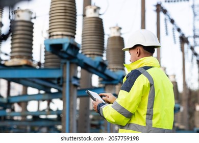 Electrical Engineer Studying Reading On Tablet. Electrical Worker Engineer A Working With Digital Tablet, Power Near Tower With Electricity. Energy Business Technology Industry Concept