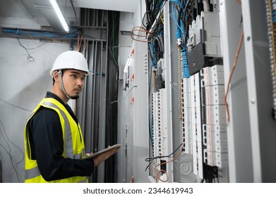 Electrical Engineer team working front control panel, An electrical engineer is installing and using a tablet to monitor the operation of an electrical control panel in a factory service room.