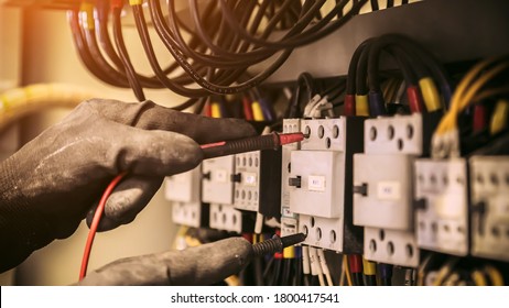 Electrical engineer using digital multi-meter measuring equipment to checking electric current voltage at circuit breaker and cable wiring system in main power distribution board.