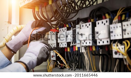 Electrical engineer using digital multi-meter measuring equipment to checking electric current voltage at circuit breaker and cable wiring system in main power distribution board.