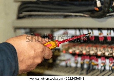 An electrical engineer's hand holding a screwdriver, reaching into an electrical box with components, performing maintenance to resolve a malfunction aboard a ship.