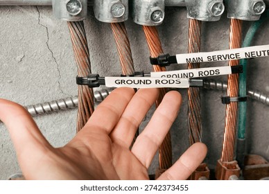 Electrical grounding and bonding busbar system. Electrician inspecting labeled grounding rods in electrical room. Copper conductors, clamps, and grounding electrodes mounted on wall. Selective focus.