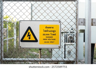Electrical high voltage caution sign plate (In Thai and English text)  that installed on wire fence of power supply station. Sign and symbol for industrial, close-up with selective focus.