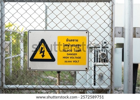 Electrical high voltage caution sign plate (In Thai and English text)  that installed on wire fence of power supply station. Sign and symbol for industrial, close-up with selective focus.