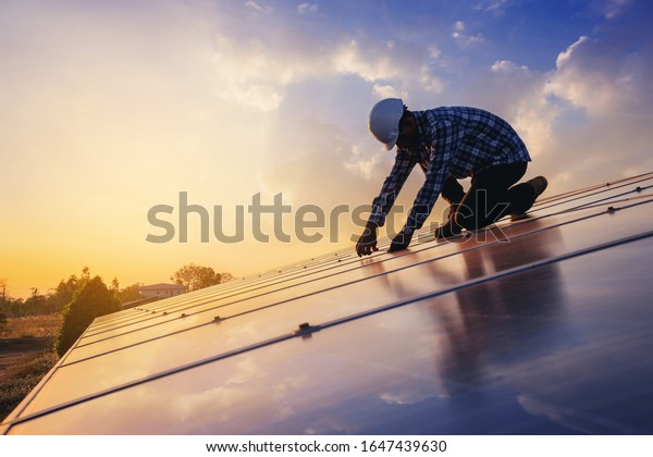 Electrical and instrument technician use\
wrench to fix and maintenance electric system at solar panel field\
with sunset sky\
reflection