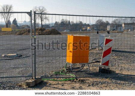 Electrical junction box in bright orange at a construction site behind a metal grid.