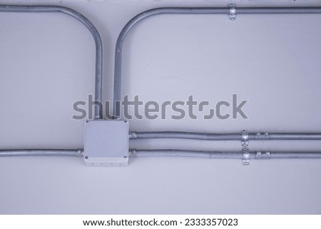 Electrical junction box and conduits on the wall. Home electrical system with electrical junction box with galvanized conduit fittings mounted on a white wall indoors. selective focus