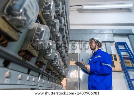 Electrical maintenance engineer checking Electricity meter and write down value of electricity on a clipboard, a smile on his face,