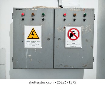 Electrical panel with indicator lights and two warning signs: danger of electric voltage and do not touch.

