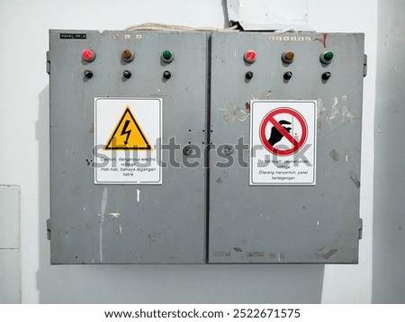 Electrical panel with indicator lights and two warning signs: danger of electric voltage and do not touch.

