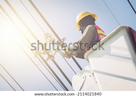Electrical power line technicians perform maintenance on power lines by using a truck-mounted bucket.