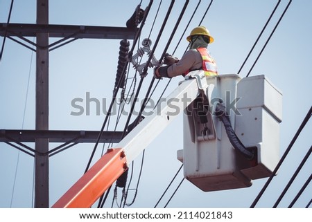 Electrical power line technicians perform maintenance on power lines by using a truck-mounted bucket.