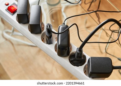 Electrical Power Strip Overloaded With Multiple Electrical Cords Plugged In. Many Plugs Plugged Into Electric Power Bar