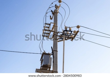 An electrical power transformer mounted on a concrete utility pole against a bright blue sky. electric grid infrastructure, energy distribution system.