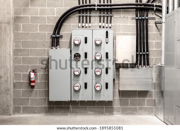 Electrical room with multiple smart meters,\
cabinets, wiring and fire extinguisher. Below-grade service room of\
4 story strata building with residential or commercial units.\
Selective focus.