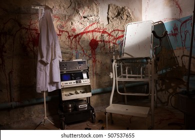 Electrical shocking device near medical gown hanging on the hanger and scary chair with blood stained wall for concept about torture or scary Halloween theme