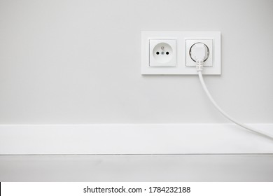 Electrical socket isolated on gray wall. White wire plug plugged in. Renovated studio apartment power supply background. Empty copy space double white plastic power outlet.