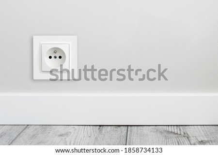 Electrical socket isolated on gray wall. Renovated studio apartment power supply background. Empty copy space single white plastic power outlet.