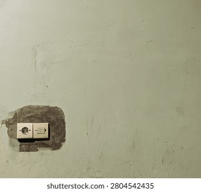 Electrical socket and light switch installed on a dark cement patch on a textured light green concrete wall