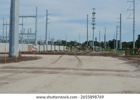 Electrical Substation Construction Site Featuring Power Lines and Equipment. Machinery and equipment. Utility poles, power lines, and soil preparation are visible, illustrating infrastructure developm
