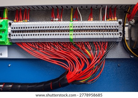 Electrical terminal block with numbered wire connections in industrial control panel, red multicore cable wiring for power distribution, engineering context for automation system switchboard assembly