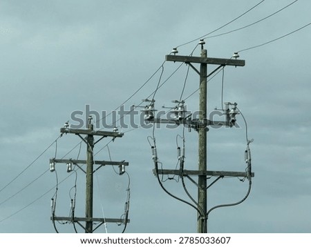 Electrical utility infrastructure with overhead power lines beneath gray cloudy sky in outdoor environment