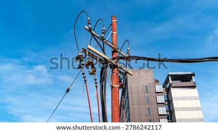 electrical utility pole with complex wiring and fuse cutouts against blue sky background, urban power grid infrastructure near apartment building