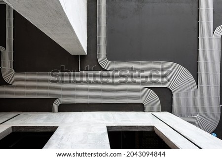 Electrical wires and pipes on house concrete ceiling background, plastic hoses with cables in empty room. Lines of pvc tubes, conduit after professional work. Renovation of home or factory interior. 