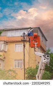 An Electrical Worker Is Repairing And Installing A Power Line At An Electric Pole. An Electrician Works On A Bucket Crane Truck Vehicle To Protect High Voltage Transmission Lines At The Electric Pole.