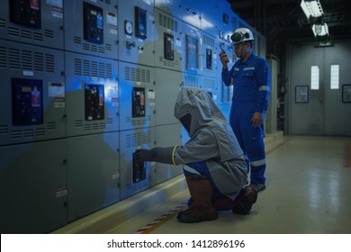 Electrical worker wearing arc flash suit protection is used to draw out a large circuit breaker. - Shutterstock ID 1412896196