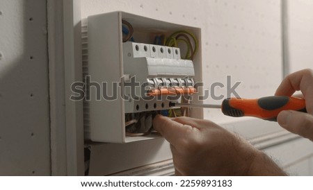 Electrician assembles electrical panel. Close up of a man hands tightening screw with a screwdriver in a switchboard high voltage electrical switches. Switch box with automatic fuses, wires, switches.
