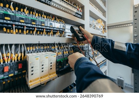 Electrician builder engineer testing and screwing equipment in fuse box and repairing of modern electricity power station using voltmeter. Automatic control cabinet