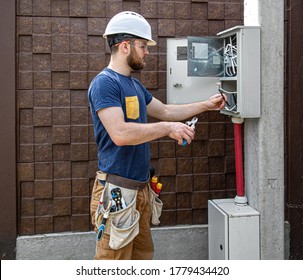 Electrician Builder at work, examines the cable connection in the electrical line in the fuselage of an industrial switchboard. Professional in overalls with an electrician's tool. 